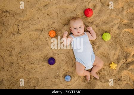 Vue de dessus d'un petit garçon heureux allongé sur une plage de sable Banque D'Images