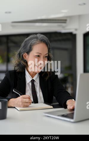 Femme d'affaires asiatique professionnelle travaillant à son bureau, utilisant un ordinateur portable et prenant des notes sur son bloc-notes. Banque D'Images