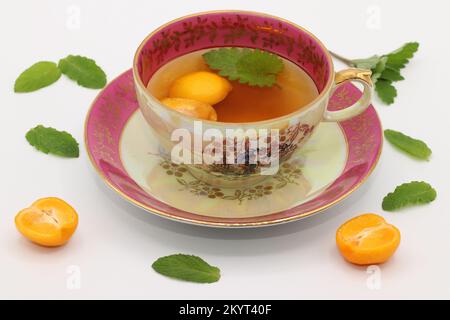 Une belle tasse de thé en porcelaine d'époque avec une feuille de melissa et des tranches de calamansi. Des feuilles de menthe et des moitiés de fruits de calamondin se trouvent autour. Agrumes microcarpa Banque D'Images