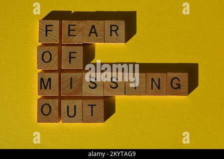 FOMO, acronyme de Fear of Missing Out, en lettres de l'alphabet en bois isolées sur fond jaune Banque D'Images