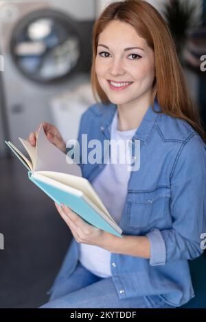 belle jeune femme lisant le livre à la laverie automatique Banque D'Images