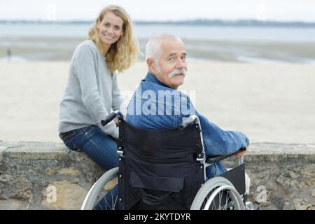 homme âgé en fauteuil roulant avec une fille adulte qui regarde la mer Banque D'Images
