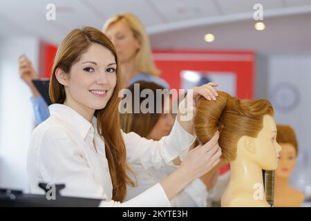 femme souriante apprenti tenant mannequin avec perruque dans le salon de coiffure Banque D'Images