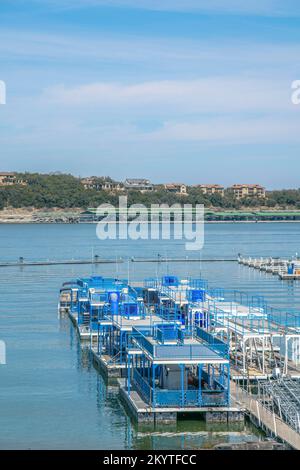 Bateaux de fête plats sur un quai à Lake Austin, Austin, Texas. Il y a une vue sur les grands bâtiments résidentiels en haut de la pente à travers le lac. Banque D'Images