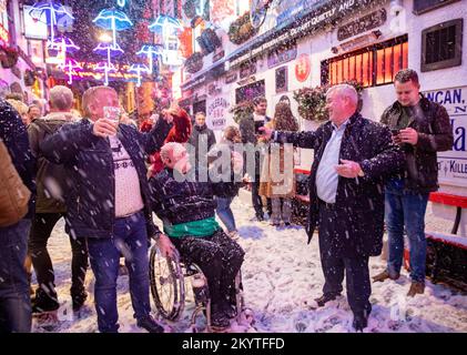 Fêtards qui chantent le long des Pogues, conte de fées de New York, alors que Guinness a donné vie à sa célèbre annonce de Noël à Belfast avec une machine à neige sur les rues pavées de commercial court devant le bar Duke of York, pendant que les invités ont été accueillis à une pinte pour commencer la saison des fêtes. Banque D'Images