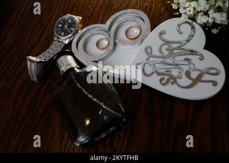 Accessoires de mariage. Invitation de mariage, une paire d'anneaux de mariage en or dans une boîte en bois en forme de coeur blanc, un bouquet de mariée, parfum, montre Banque D'Images