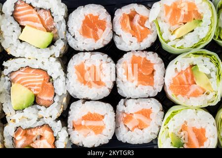 Vue de dessus d'un plateau à emporter de makis de saumon de différents types. Cuisine orientale et japonaise. À emporter. Prise de vue avec objectif macro. Banque D'Images