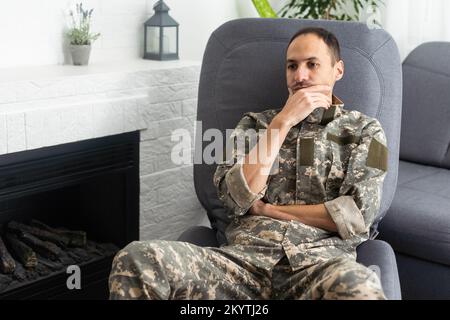 Un militaire attentionné, tenant les paumes par la bouche, assis sur un canapé à la maison. Jeune soldat visitant psychologue, souffrant de Banque D'Images