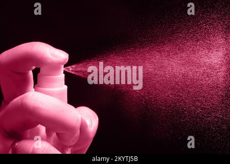 L'homme arrose un spray de parfum sur fond noir. Couleur de l'année 2023 Viva Magenta Banque D'Images