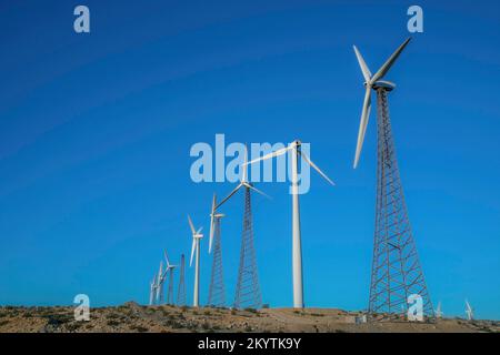 Moulin à vent avec des tours tubulaires en acier et en treillis dans une rangée sur un désert en Californie. Éoliennes sur un terrain déserté contre le ciel bleu clair backgro Banque D'Images