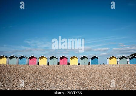 Une rangée de plages aux couleurs vives s'étend sous un ciel bleu ensoleillé sur une plage déserte de galets à Eastbourne Banque D'Images