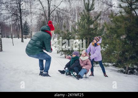 Photo de joli petit enfant funky femme mari manteaux vêtus traîneaux s'amuser ensemble à l'extérieur parc forestier urbain Banque D'Images