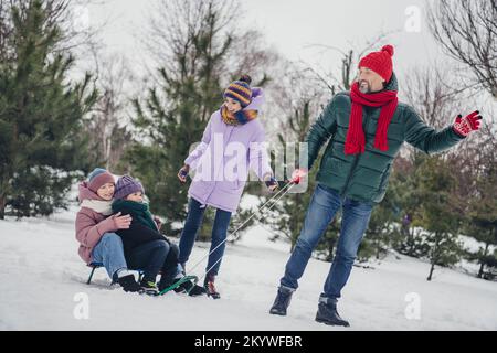 Photo de charmant mari excité femme petit enfant porter coupe-vent traînant traîneaux s'amuser ensemble à l'extérieur du parc urbain Banque D'Images