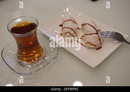 Déjeuner sucré avec gâteau, gelée de fruits et thé dans un verre sur une table blanche, cuillères à café Banque D'Images