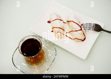 Déjeuner sucré avec gâteau, gelée de fruits et thé dans un verre sur une table blanche, cuillères à café Banque D'Images