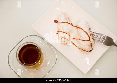 Déjeuner sucré avec gâteau, gelée de fruits et thé dans un verre sur une table blanche, cuillères à café Banque D'Images