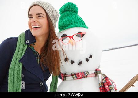 Hiver, neige et femme heureuse embrassant un bonhomme de neige à Noël à l'extérieur de l'Angleterre en souriant. Fêtes, fêtes de fin d'année et fêtes de Noël ou tradition avec Banque D'Images