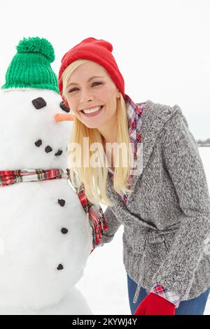 Portrait, hiver et femme avec un bonhomme de neige pendant Noël, dehors dans la neige au Royaume-Uni. Visage, devant et femme avec bonhomme de neige en Noël ou en fête Banque D'Images