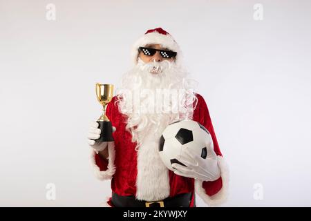 le père noël avec des lunettes de soleil 'thug life' ballon de football et un trophée dans sa main sur fond blanc Banque D'Images