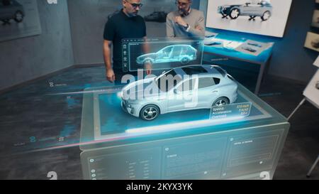 Deux ingénieurs les développeurs qui se trouvent dans un studio de conception près d'une table holographique futuriste et font un test dans un simulateur d'essai de collision de voiture 3D, qui simule un accident de la route, vérifient la sécurité Banque D'Images