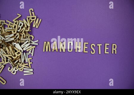 Pile de lettres majuscules en bois de langue anglaise qui se répande en mots - MANCHESTER avec un fond violet Banque D'Images