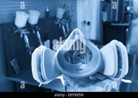 Respirateur professionnel dans un atelier de réparation automobile avec pistolets de pulvérisation sur fond Banque D'Images