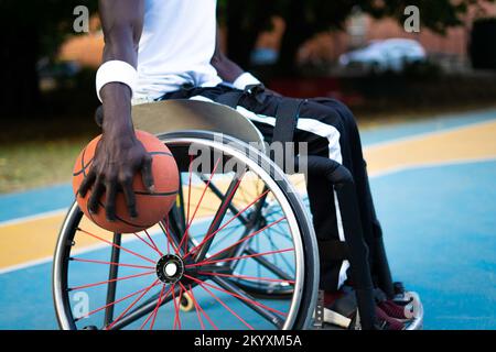 Un athlète champion ayant un handicap jouant au basket-ball en extérieur. Portrait de l'homme afro-américain avec balle regardant l'appareil photo et souriant. Concept de Banque D'Images