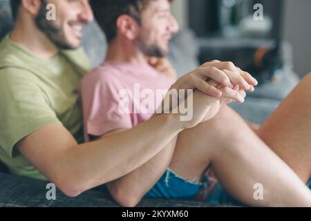 Jeunes heureux gay lgbtq couple mains tenant à la maison assis sur le canapé - couple gay regardant la télévision assis sur le canapé et s'amuser - filtre d'époque Banque D'Images