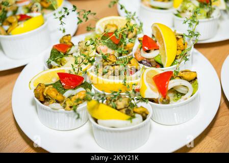 Moules avec une tranche de citron et de microverts, rondelles de calmar et sauce pesto dans des ramequins, plusieurs portions Banque D'Images