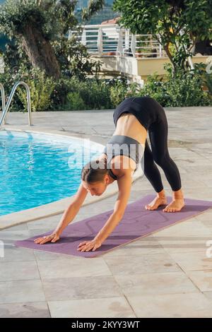 Jeune femme pratiquant le yoga au bord de la piscine en soirée. Banque D'Images