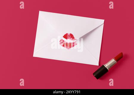 Rouge à lèvres baiser sur enveloppe blanche sur fond magenta. Concept de lettre d'amour. Tendance des couleurs année 2023. Banque D'Images