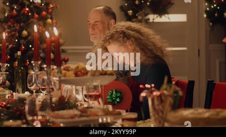 Bonne famille multi-culturelle célébrant Noël ou nouvel an 2023, échanger des cadeaux. Servi table de vacances avec différents plats et bougies. Ambiance chaleureuse du dîner de Noël familial à la maison. Banque D'Images