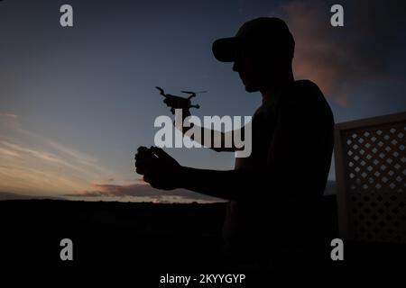 Silhouette d'un pilote de drone sur le point de faire voler son drone au coucher du soleil Banque D'Images