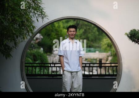 Mignon petit homme chinois souriant à la porte de lune dans un jardin de style chinois traditionnel. Vue avant Banque D'Images