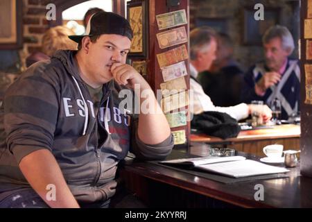 Que dois-je commander ? Portrait d'un jeune homme assis seul au bar. Banque D'Images