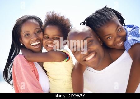 La taille de leurs sourires montre à quel point ils sont heureux. Deux parents donnent à leurs enfants un porcgyback pendant qu'ils sont sur la plage.