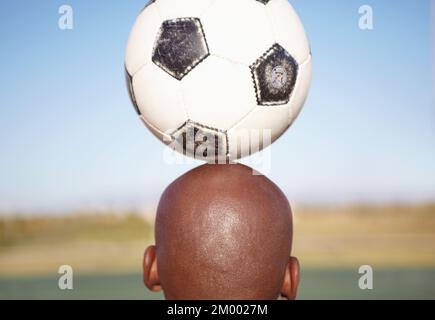 Équilibre et compétence. Image courte d'un homme qui équilibre un ballon de football sur sa tête. Banque D'Images