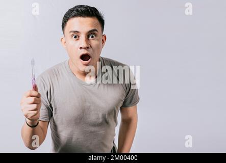 Un homme tenant une brosse à dents avec un visage émerveillé isolé sur blanc, surpris un jeune homme tenant une brosse à dents. Un adolescent stupéfié tenant la brosse à dents isolée Banque D'Images