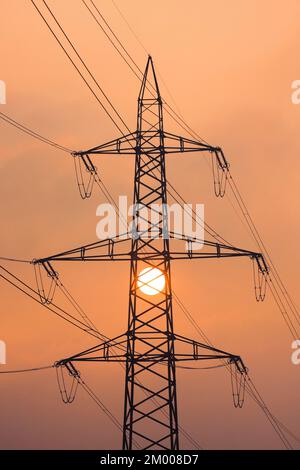 Coucher de soleil derrière la silhouette de pylônes de ligne haute tension, enveloppés de lumière orange dans le brouillard, Canton de Zurich, Suisse, Europe Banque D'Images