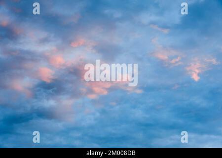 Des nuages roses bordent le ciel bleu du soir au coucher du soleil Banque D'Images