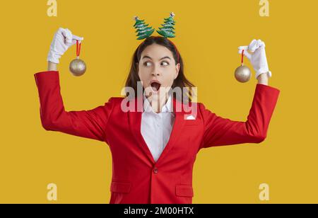 Drôle surprise femme en costume rouge et serre-tête festif tenant des boules d'arbre de Noël Banque D'Images