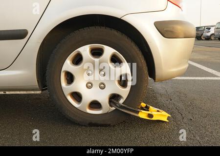 Le petit collier de serrage de roue Yelllow fixe le dessus du pneu arrière d'une voiture grise dans un stationnement Banque D'Images