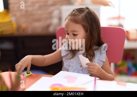 Adorable étudiante hispanique de fille assise sur le papier de découpe de table à la maternelle Banque D'Images