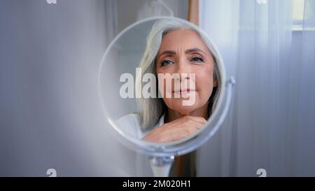 Miroir réflexion femme ridée visage 50s d'âge moyen femme caucasienne senior dame regardant l'auto-amant soin de peau grand-mère pensant se faire dorloter Banque D'Images