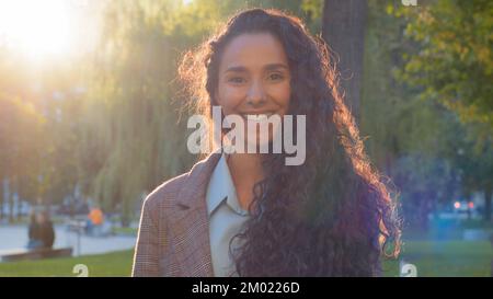 Portrait de femme à l'extérieur beau sourire gai insouciant jeune femme brune fille dame avec de longs cheveux bouclés et des dents blanches tient au soleil Banque D'Images