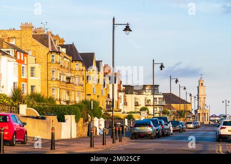 Le Central Parade en bord de mer déserté, le matin de l'été, à Herne Bay, dans le Kent. Voitures garées le long de la route, rangée de maisons en bord de mer et tour de l'horloge. Banque D'Images