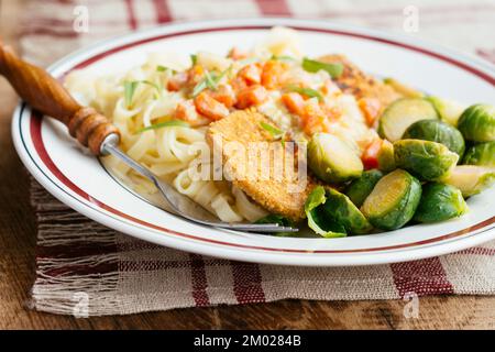 Schnitzel aux légumes sur des nouilles avec une sauce crémeuse à l'estragon et des choux de Bruxelles. Banque D'Images