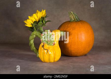 Un seul tournesol dans une broche en céramique ou picher, avec une tarte au sucre citrouille en arrière-plan. Banque D'Images