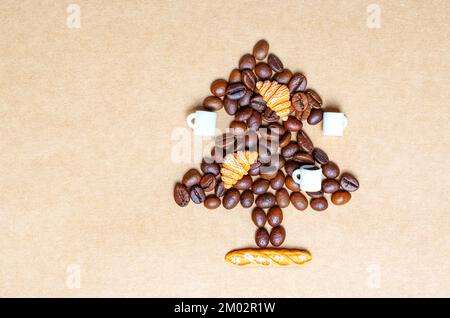 Forme d'arbre de Noël faite à partir de grains de café torréfiés foncés, de petites tasses de café et de croissants sur un fond de papier artisanal. Banque D'Images