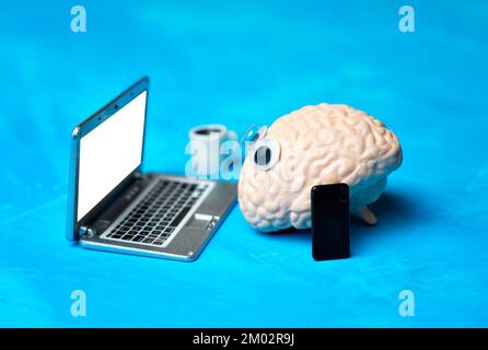 Copie anatomique d'un cerveau humain avec googly oui travaillant sur un ordinateur portable miniature isolé sur fond bleu. Concept créatif lié à l'emploi de bureau. Banque D'Images